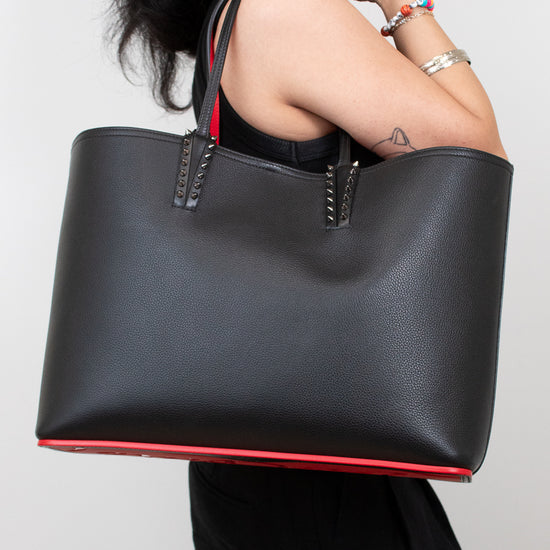 Person holding a black handbag with red bottom trim & inner strap against a plain background