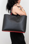 Person holding a black handbag with red bottom trim & inner strap against a plain background