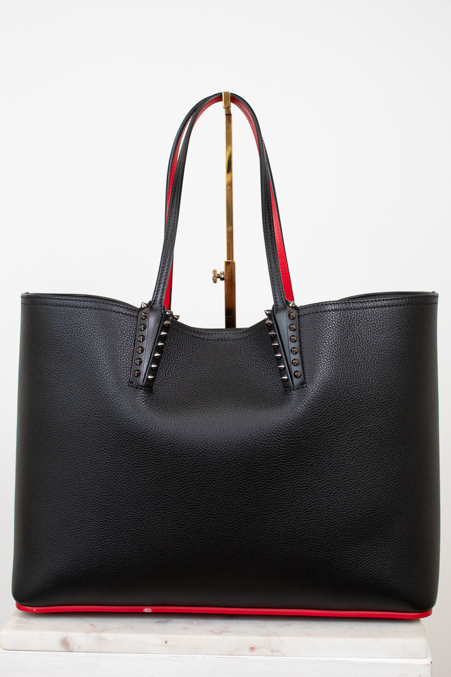 Black leather tote bag with red accents and gold spike accents on handle on a white background