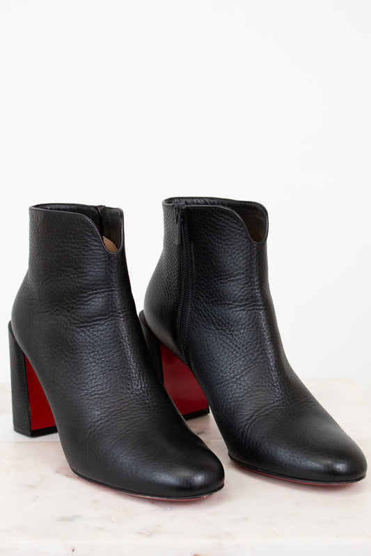Pair of black ankle boots with red soles on a light background