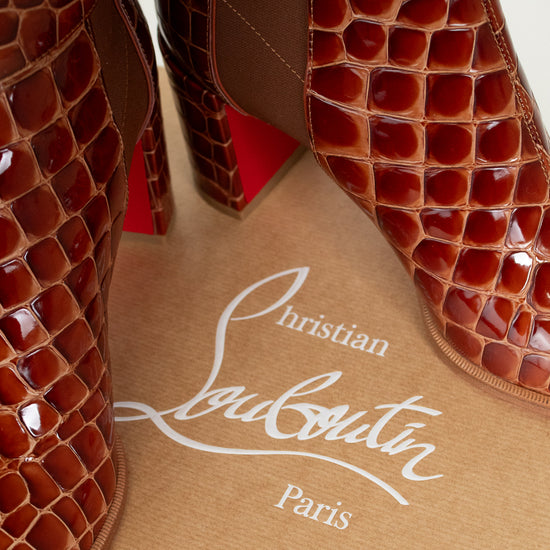 Brown crocodile-patterned high-heeled shoes on a beige surface with Christian Louboutin branding.
