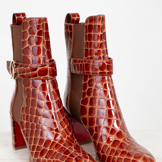 Pair of brown crocodile-patterned high-heeled boots on a light background