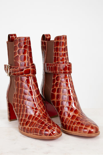 Pair of brown crocodile-patterned high-heeled boots on a light background