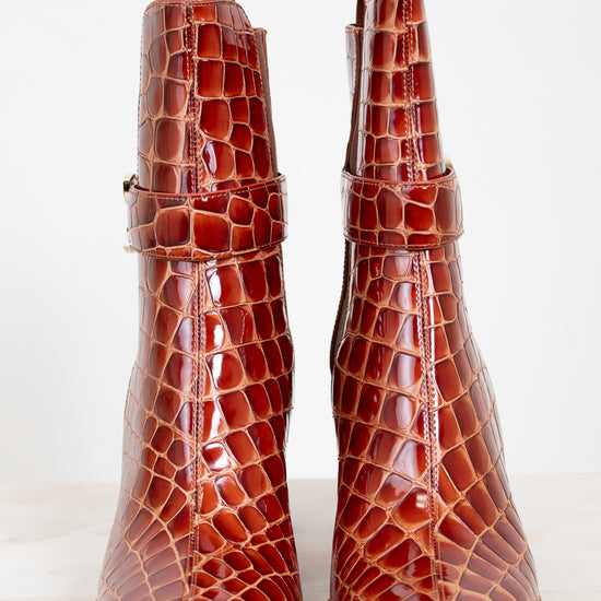 Pair of brown crocodile-patterned boots on a white background