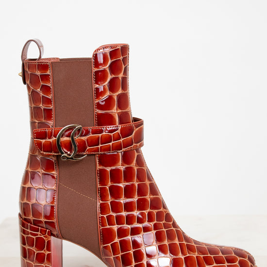 Brown crocodile-patterned boot with a buckle on a white background