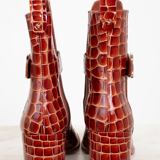 Pair of brown crocodile-patterned boots on a white background