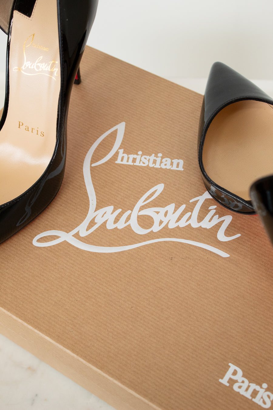 Black high-heeled shoes on a brown Christian Louboutin box with white logo.