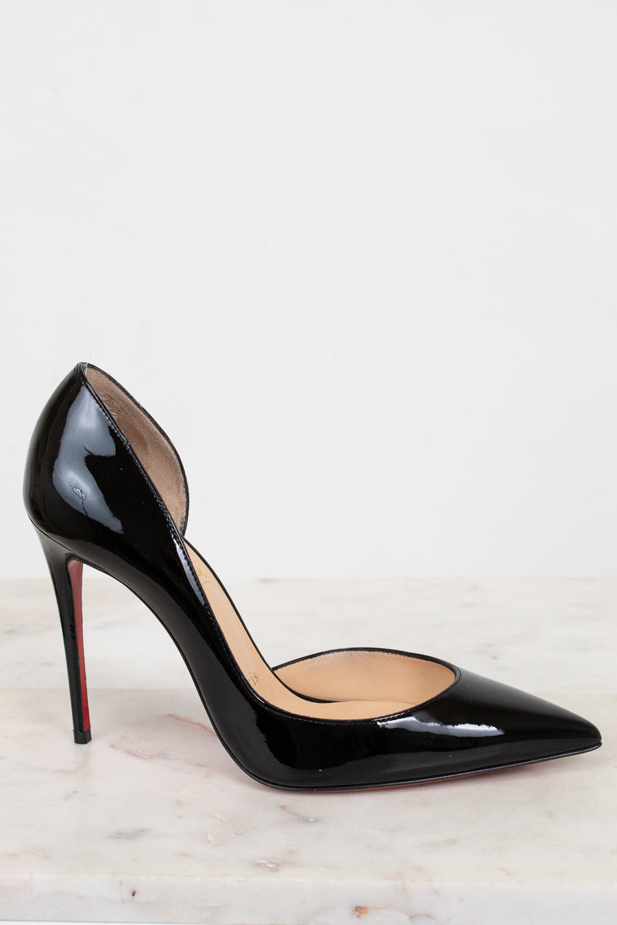 Black high-heeled shoe with a red sole on a light background