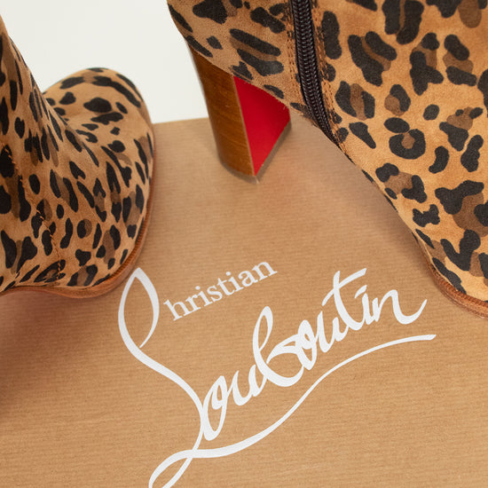 Leopard print boots with a red sole on a beige surface featuring Christian Louboutin branding.