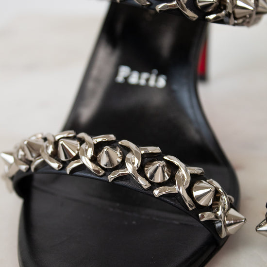 Black sandal with silver chain detail on a light background