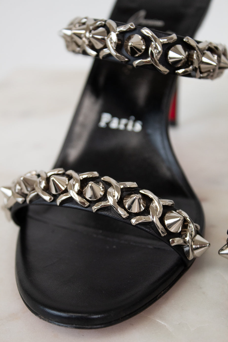 Black sandal with silver chain detail on a light background