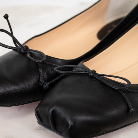 Black ballet flats with bow details on a light wooden surface
