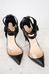 A pair of black pointed-toe high heels with PVC panel and ankle straps, shown on a light marble surface against a white background.