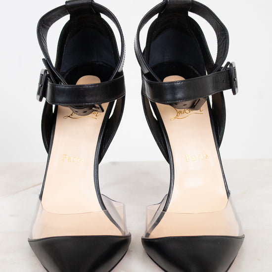 A pair of black pointed-toe high heels with clear side panels and ankle straps, shown on a light marble surface against a white background.