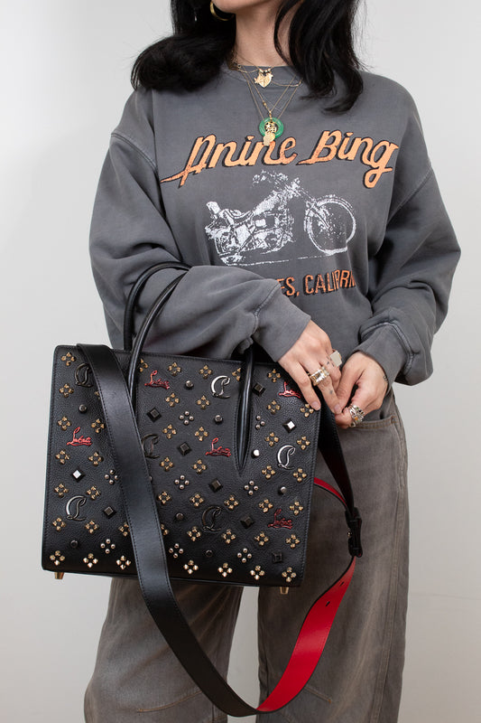 Person wearing a gray sweatshirt with text, holding a black studded handbag with red strap.