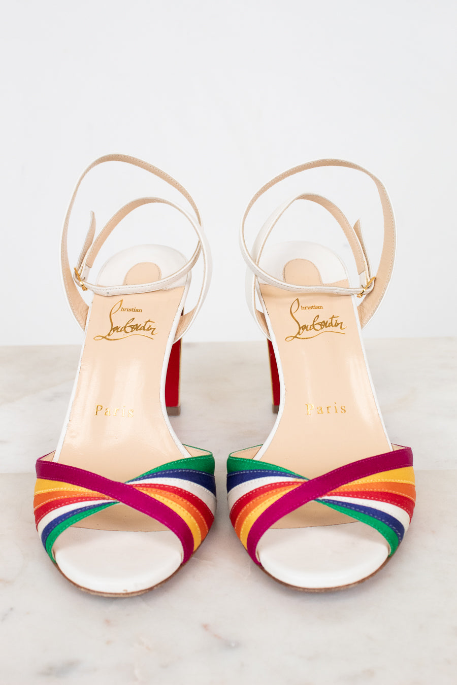 Pair of white heels with rainbow-striped detail with brand name on a light background