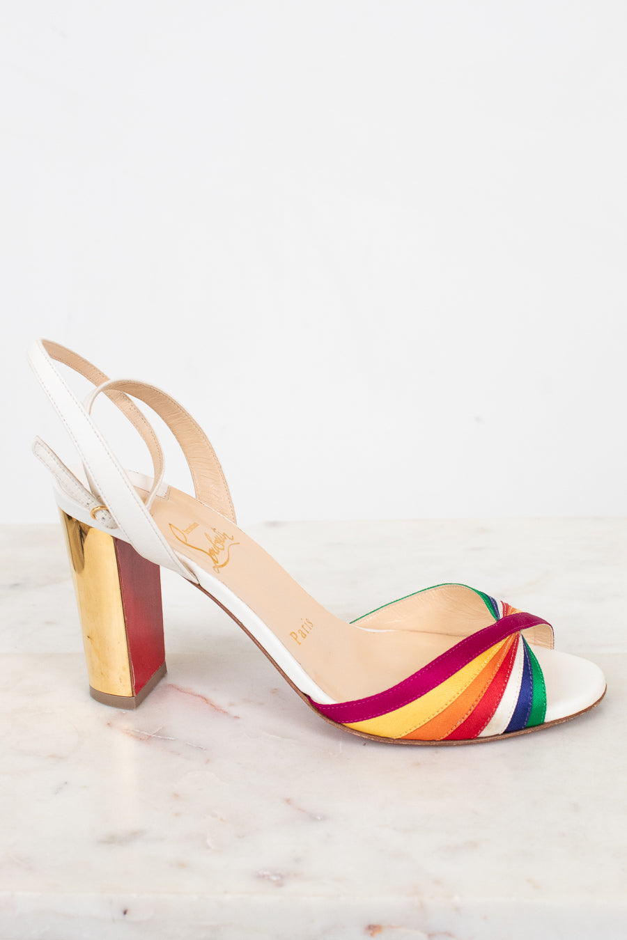 White sandal with a rainbow strap and gold chunky heel on a white background