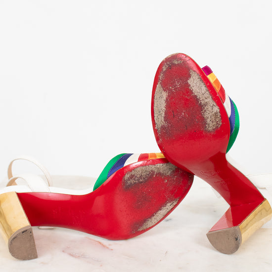 Worn red bottom high-heeled shoes with rainbow accents on a white background