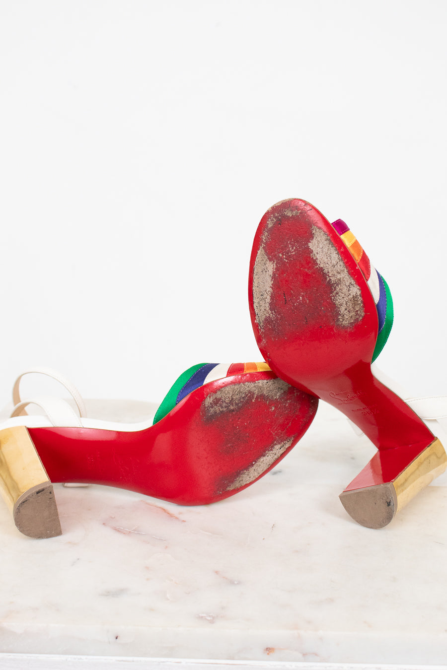 Worn red bottom high-heeled shoes with rainbow accents on a white background