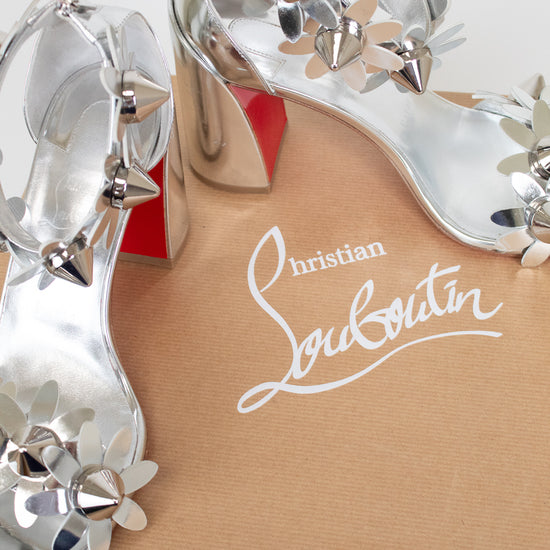Close-up of a Christian Louboutin shoe with decorative silver studded flowers on a white background