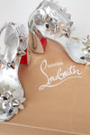 Close-up of a Christian Louboutin shoe with decorative silver studded flowers on a white background