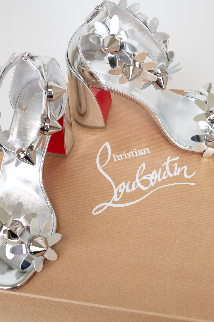 Close-up of a Christian Louboutin shoe with decorative silver studded flowers on a white background