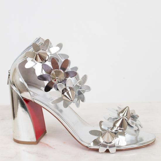 Silver high-heeled shoes with studded floral designs on a white background