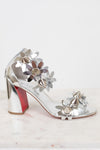 Silver high-heeled shoes with studded floral designs on a white background