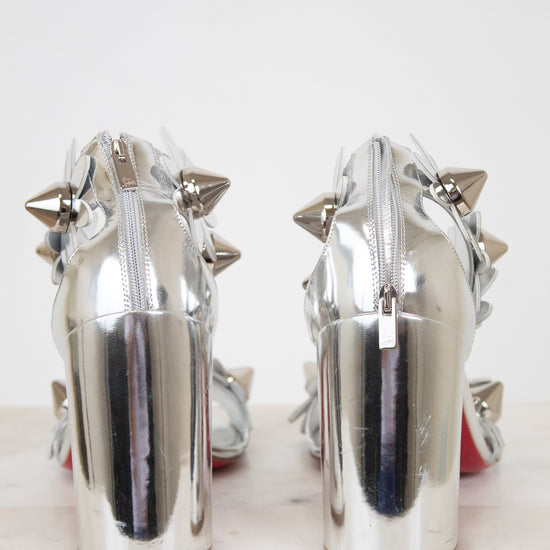 Pair of silver high-heeled shoes with studded details on a white background