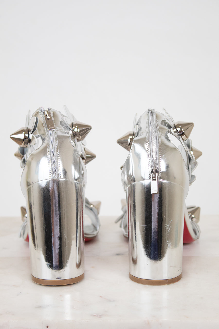 Pair of silver high-heeled shoes with studded details on a white background
