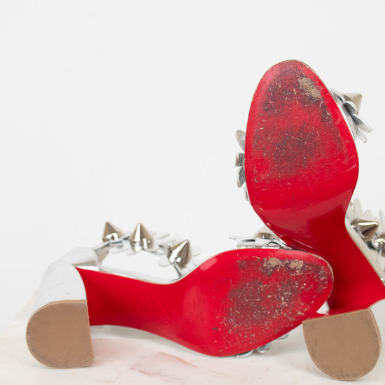 Bottom soles of red high-heeled shoes with studded details on a white background