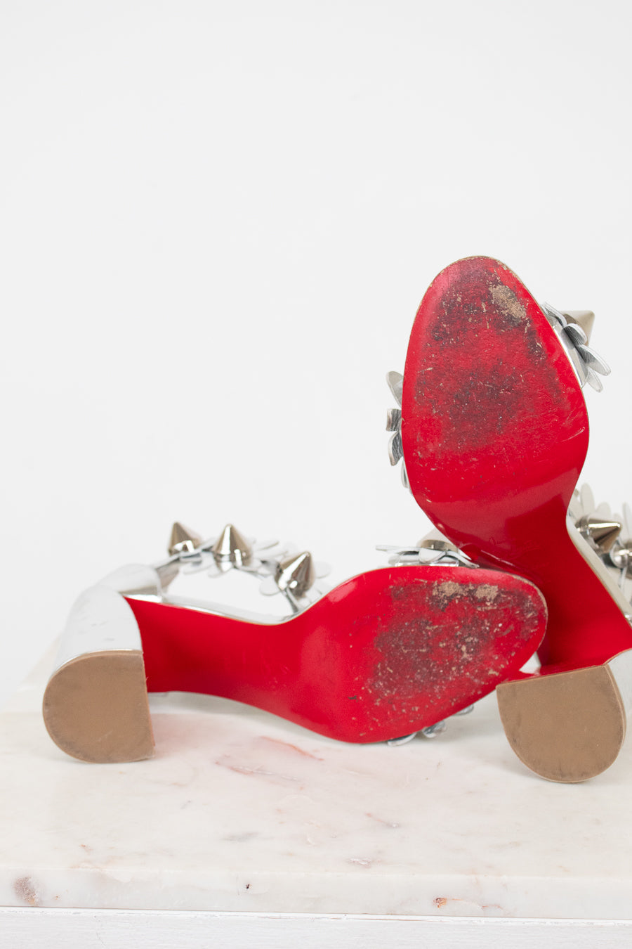 Bottom soles of red high-heeled shoes with studded details on a white background