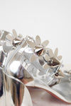 Silver high-heeled shoes with floral studded embellishments on a light background