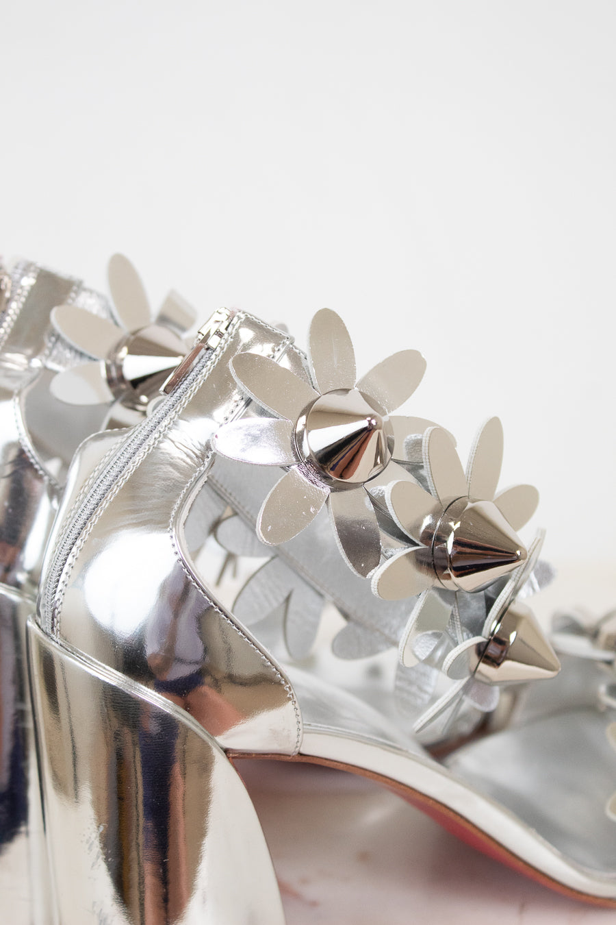 Silver high-heeled shoes with floral studded embellishments on a light background
