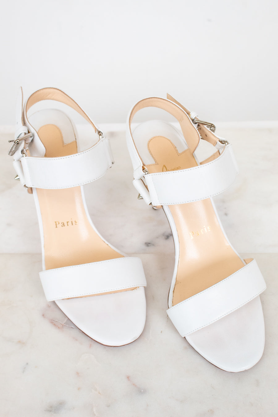 White high-heeled sandals with a brand name on a light background