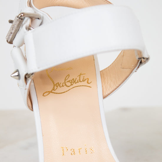 White high-heeled shoe with beige insole and 'Louboutin Paris' branding on a light gray background