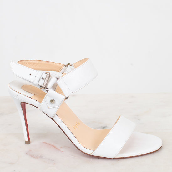 White high-heeled sandal with a red sole on a light gray background