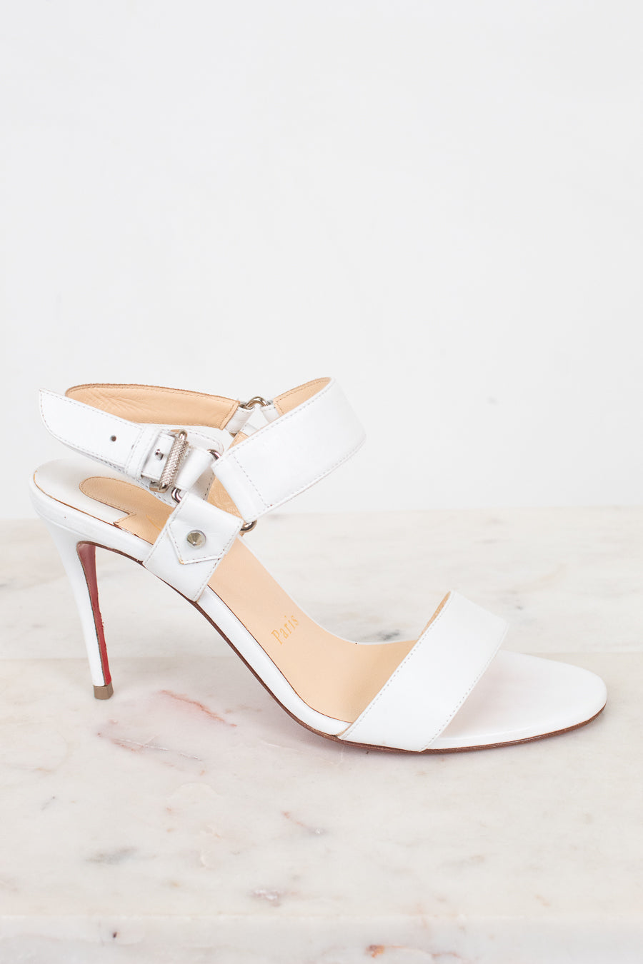 White high-heeled sandal with a red sole on a light gray background