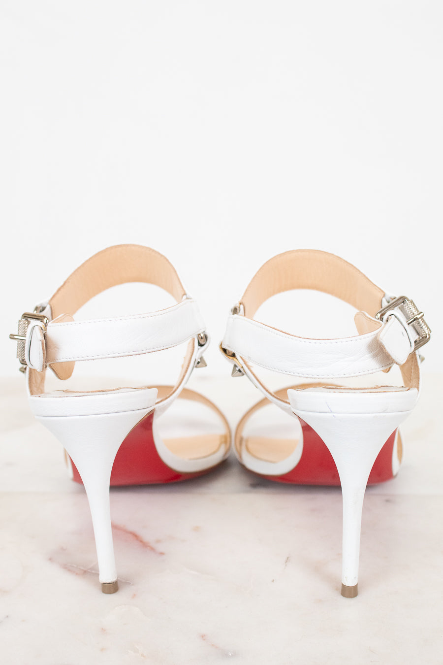 White high-heeled shoes with red bottom soles on a light background
