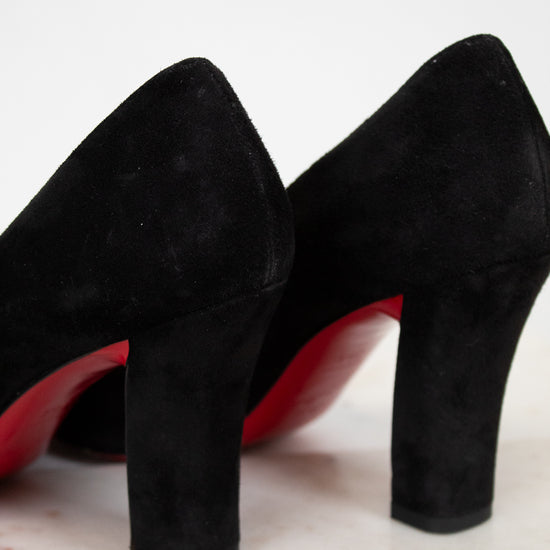 Black high-heeled shoes with red soles on a light wooden surface.