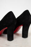 Black high-heeled shoes with red soles on a light wooden surface.