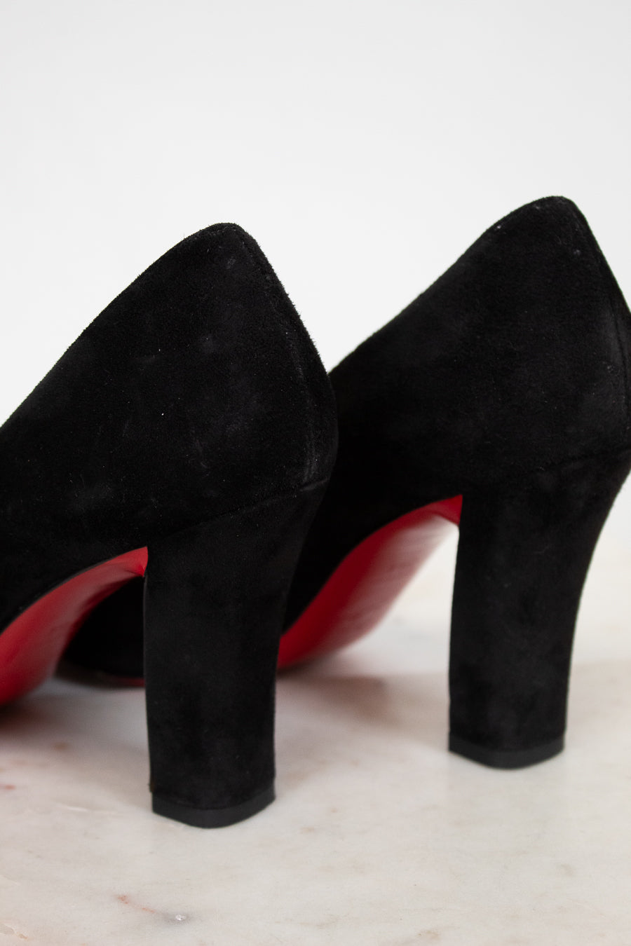 Black high-heeled shoes with red soles on a light wooden surface.