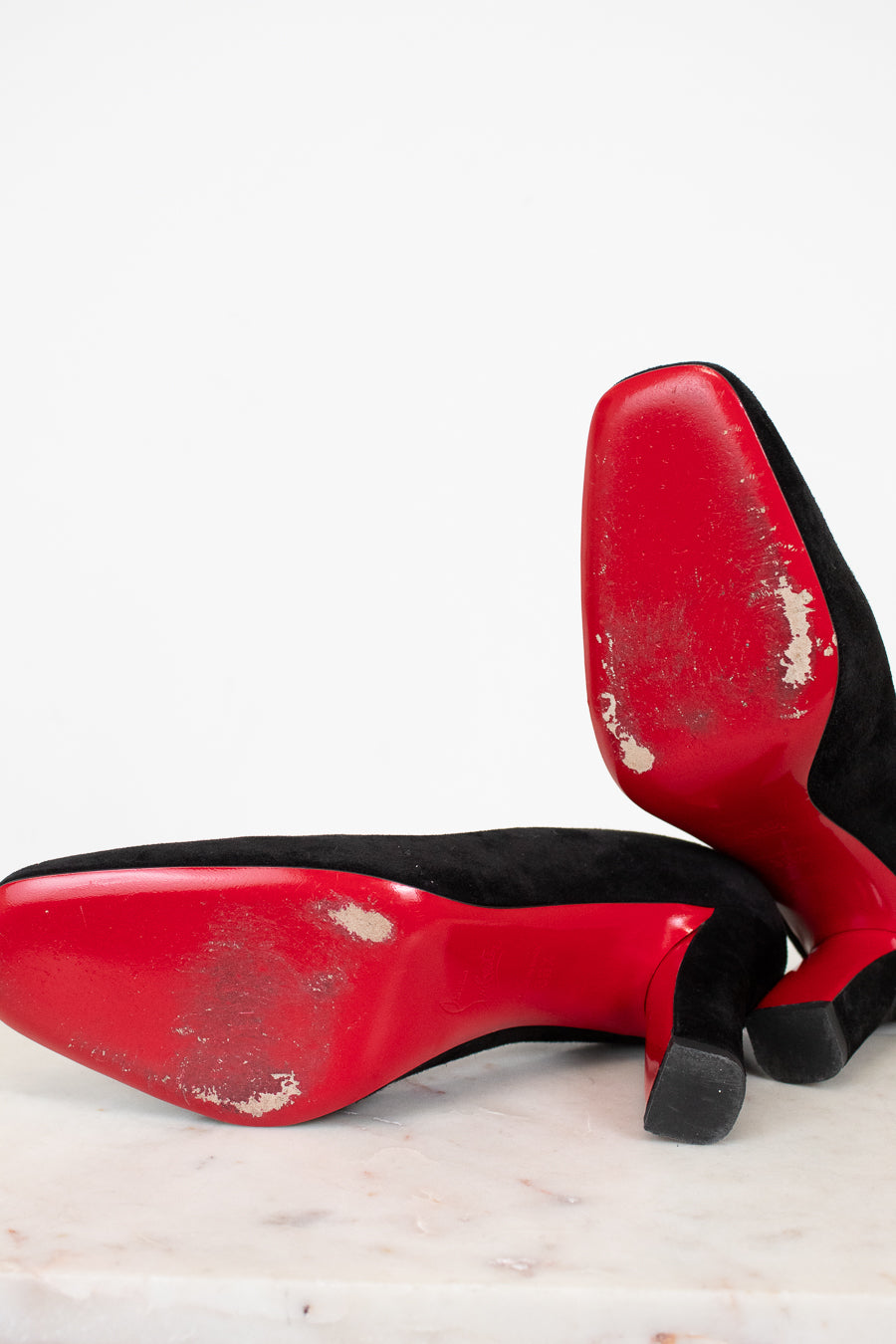Red high-heeled shoes with black soles on a light marble surface.