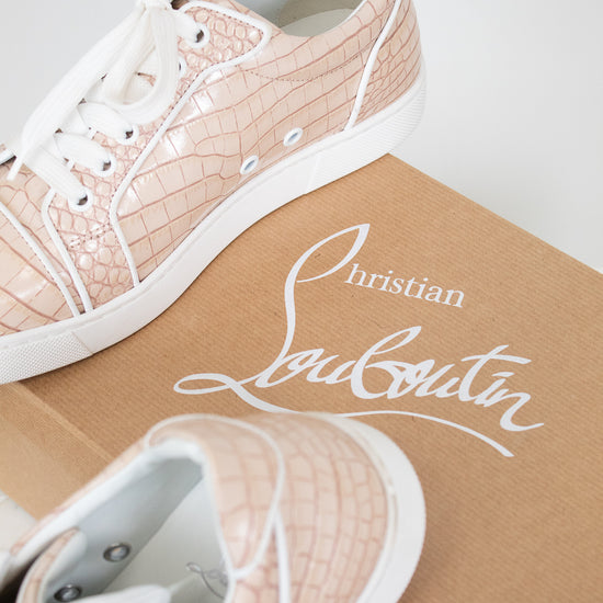 Pink crocodile-patterned sneakers with white soles on a Louboutin branded box.
