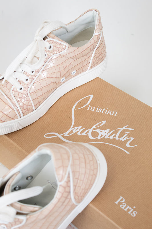 Pink crocodile-patterned sneakers with white soles on a Louboutin branded box.