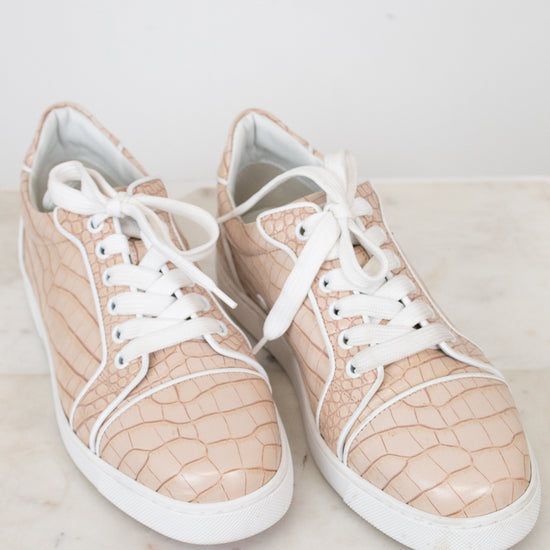 Pair of beige crocodile print sneakers with white laces on a light surface
