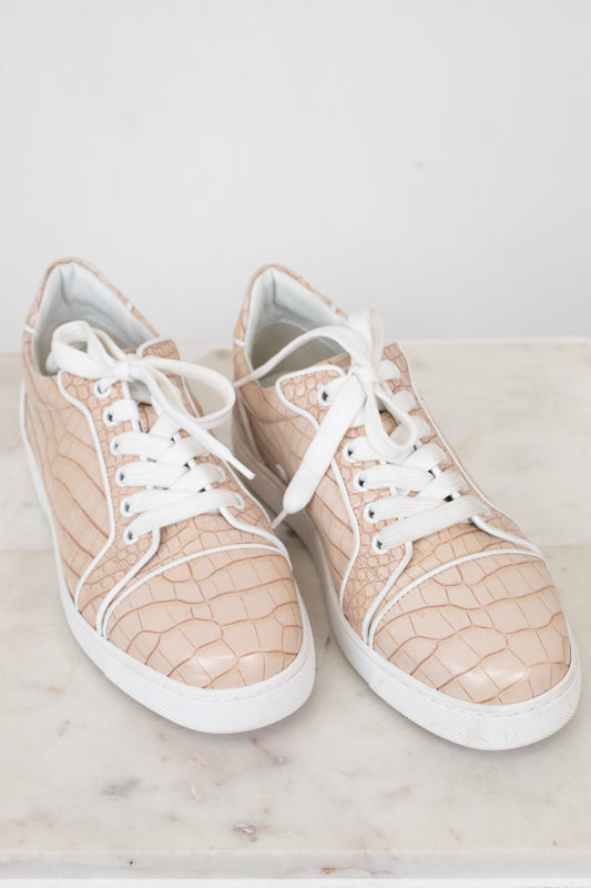 Pair of beige crocodile print sneakers with white laces on a light surface