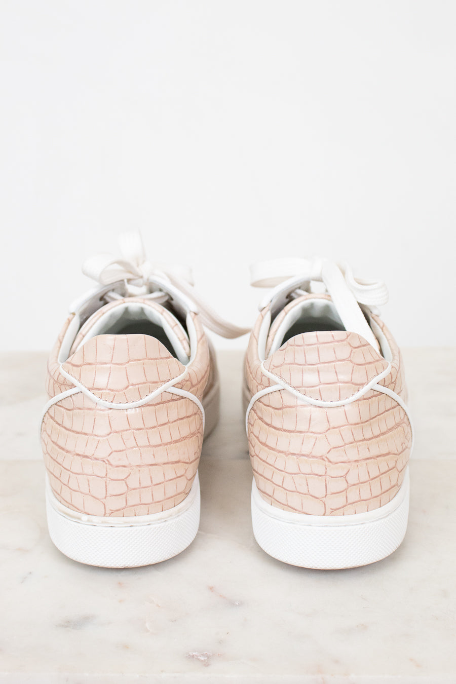 Pair of light pink crocodile-patterned sneakers on a white background