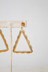 Gold triangular dangle earrings with a textured beaded border, displayed on a beige fabric jewelry stand against a light gray background.