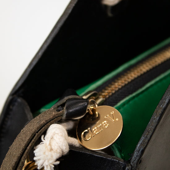 Close-up of a 'Clare V.' gold tag on a black leather handbag.